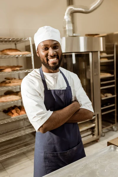 Lächelnder afrikanisch-amerikanischer Bäcker mit verschränkten Armen bei der Herstellung von Backwaren — Stockfoto