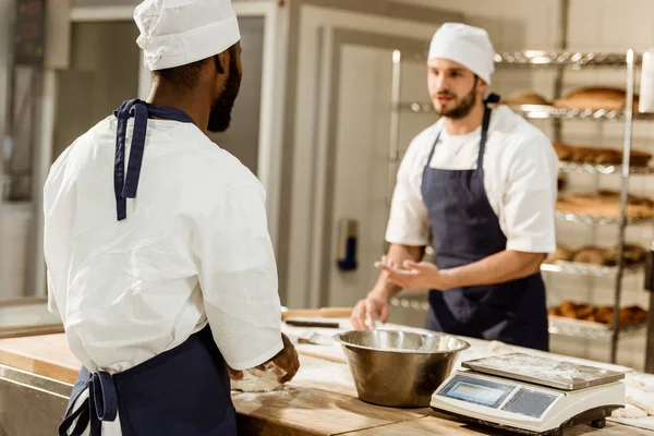 Bakers in uniform kneading dough together at baking manufacture — Stock Photo