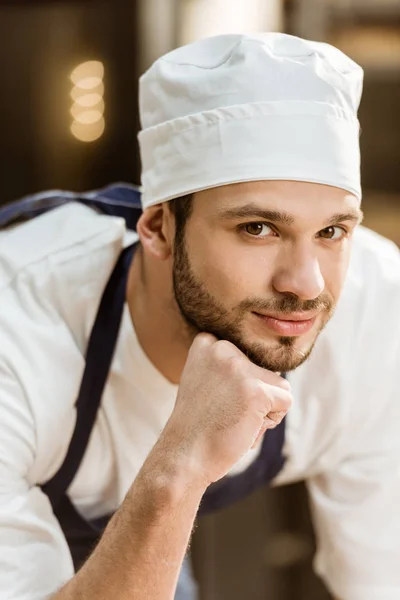 Nahaufnahme Porträt eines hübschen jungen Bäckers, der bei der Herstellung von Backwaren in die Kamera schaut — Stockfoto