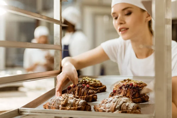 Beautiful female baker holding tray of freshly baked croissants on baking manufacture — Stock Photo