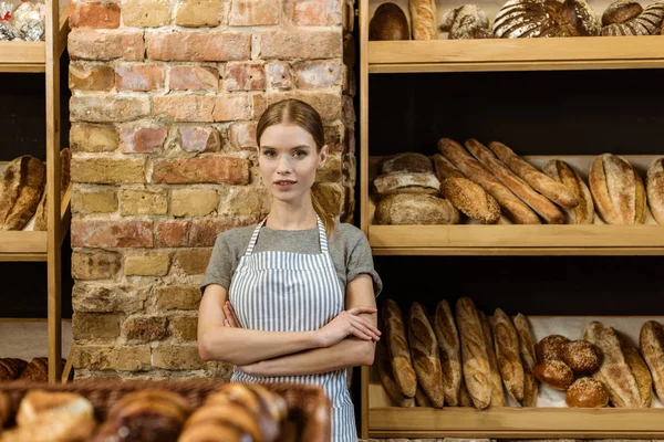 Hermoso panadero joven con brazos cruzados de pie en la pastelería - foto de stock