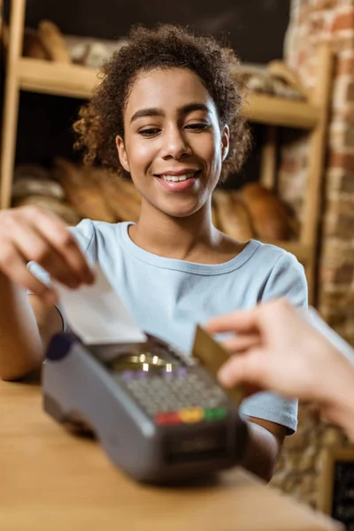 Nahaufnahme einer glücklichen Kassiererin mit POS-Terminal, die beim Kunden in der Konditorei einkauft — Stockfoto