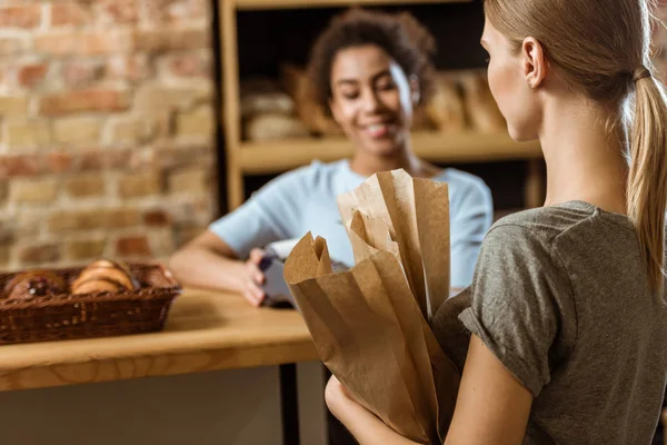 Mujer joven con bolsas de papel en la pastelería - foto de stock