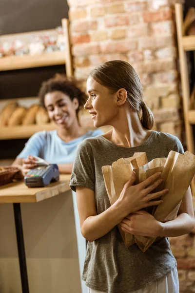Glückliche junge Frau verlässt Konditorei mit verschiedenen Broten in Papiertüten — Stockfoto