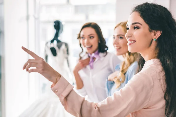 Young smiling bride and bridesmaids choosing dresses in wedding fashion shop — Stock Photo