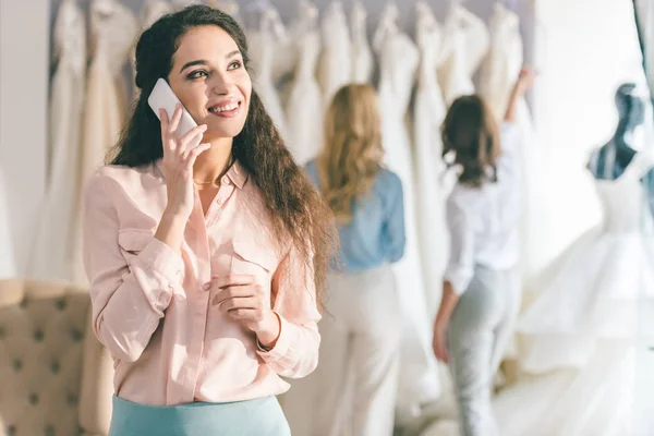 Woman talking on phone while choosing dress in wedding salon — Stock Photo