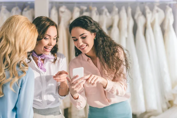 Hermosa novia y amigas mirando la pantalla del teléfono en el salón de bodas - foto de stock