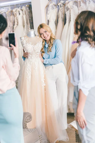 Damas de honor y novia tomando fotos al elegir el vestido en la tienda de moda de boda - foto de stock