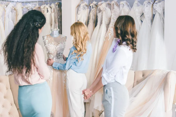Noiva feliz e damas de honra experimentando vestidos no atelier de casamento — Fotografia de Stock