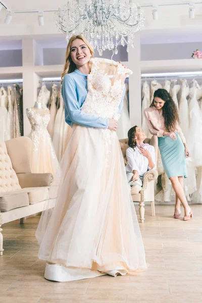 Laughing bride and bridesmaids trying on dresses in wedding atelier — Stock Photo