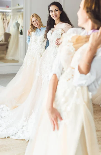 Novias jóvenes sosteniendo vestidos en el taller de la boda - foto de stock