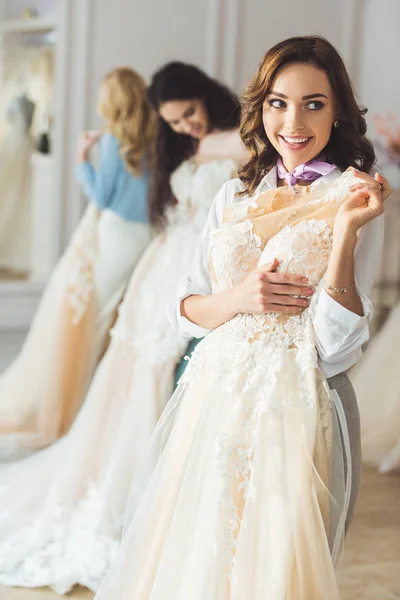 Lächelnde Frauen mit Brautkleidern im Hochzeitssalon — Stockfoto