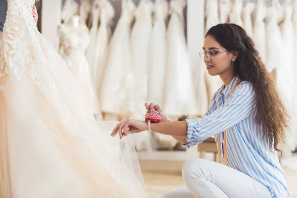 Costurera trabajando por hermoso vestido en atelier de boda - foto de stock