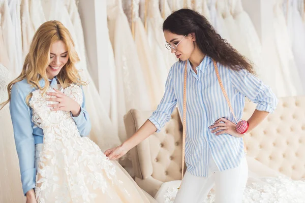 Braut hält Kleid von Schneiderin im Hochzeitssalon — Stockfoto