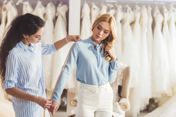 Jovem mulher e alfaiate profissional tomando medidas na loja de moda do casamento — Fotografia de Stock