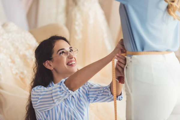 Tailor measuring waist of female client in wedding fashion shop — Stock Photo