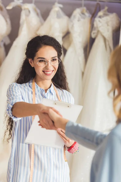 Alfaiate feminino e noiva apertando as mãos na loja de moda do casamento — Fotografia de Stock