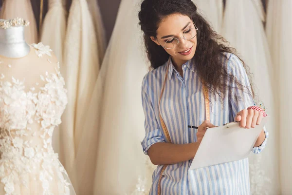 Портной письма в буфер обмена красивым платьем в свадебном магазине моды — стоковое фото