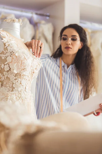 Tailor attaching decorative details to dress in wedding salon — Stock Photo