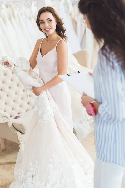 Braut mit Kleid und Schneiderschrift im Klemmbrett im Hochzeitsatelier — Stockfoto