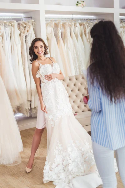 Female tailor by bride trying on wedding dress in wedding salon — Stock Photo
