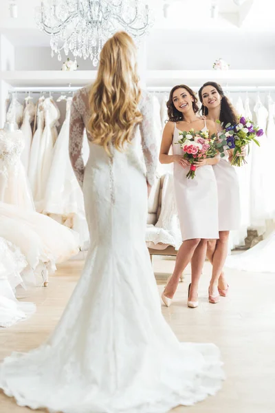 Brautjungfern mit Blumen betrachten die schöne Braut im Hochzeitsatelier — Stockfoto