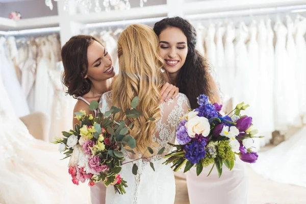 Atractiva novia y damas de honor abrazándose en el atelier de bodas - foto de stock