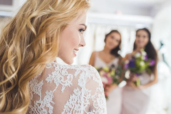 Novia en vestido de encaje y damas de honor con flores en la tienda de moda de boda - foto de stock