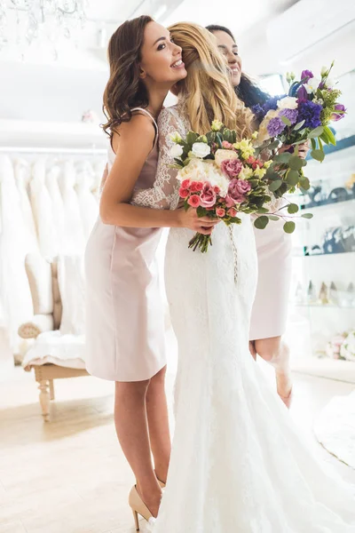 Mulheres sorridentes em vestidos de noiva abraçando no atelier de casamento — Fotografia de Stock