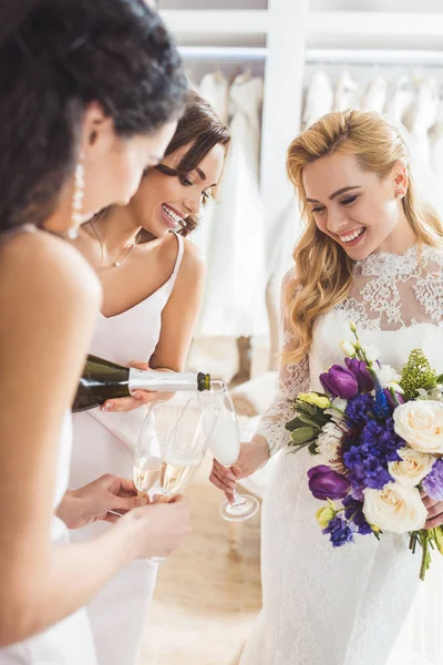 Mujeres atractivas en vestidos de novia vertiendo champán en la tienda de moda de boda - foto de stock