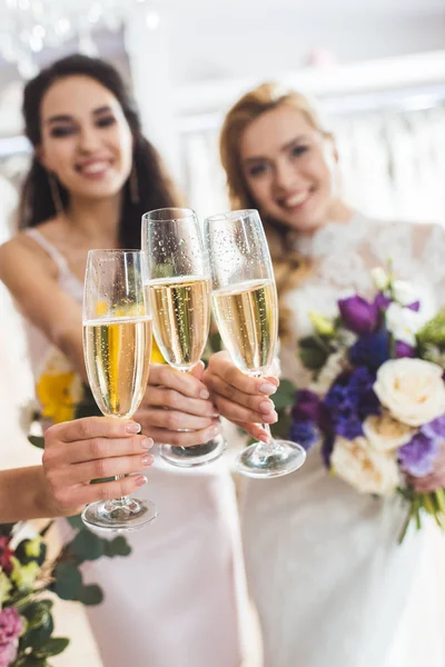 Joven sonriente novias con champán en copas en atelier de bodas - foto de stock