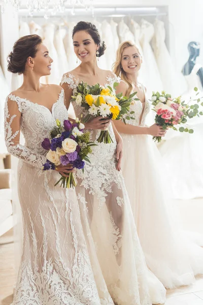 Mulheres sorridentes em vestidos de noiva com flores no atelier de casamento — Fotografia de Stock