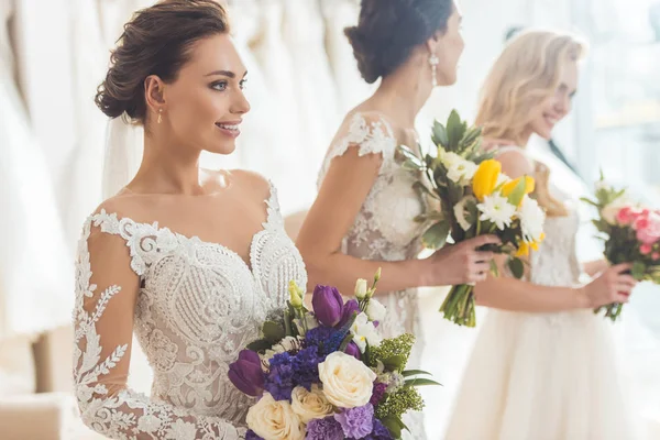 Junge lächelnde Bräute mit Sträußen im Geschäft für Hochzeitsmode — Stockfoto