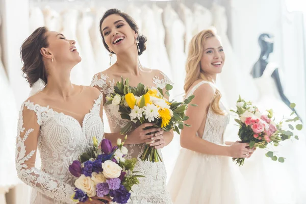 Mujeres felices en vestidos de novia con flores en el taller de bodas - foto de stock