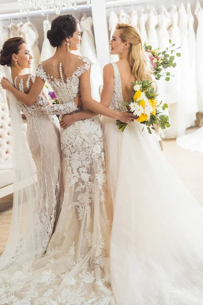 Привлекательные женщины в свадебных платьях, обнимающиеся в свадебном магазине — стоковое фото