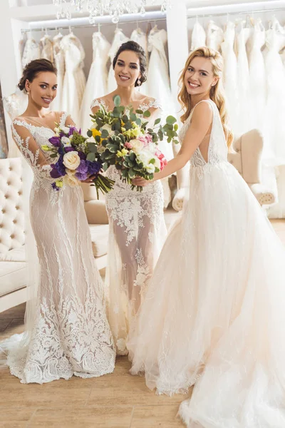Счастливые женщины в свадебных платьях с цветами в свадебном салоне — стоковое фото