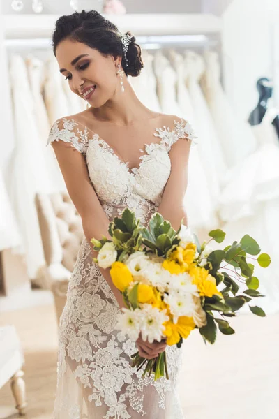 Novia sonriente con flores en la tienda de moda de boda - foto de stock