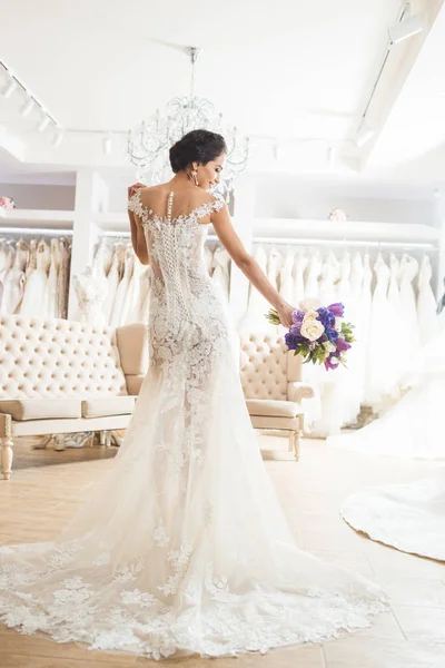 Hermosa novia con ramo de flores en la tienda de moda de boda - foto de stock