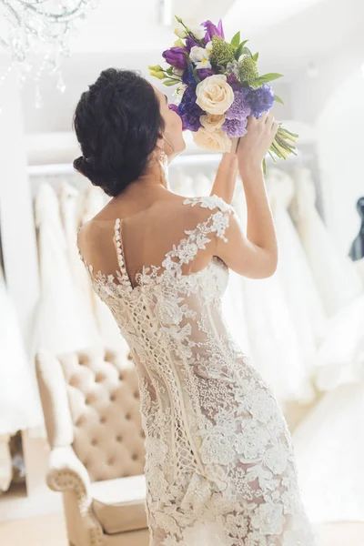 Rear view of bride in lace dress with flowers in wedding atelier — Stock Photo