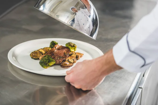 Abgeschnittenes Bild des Chefs, der Teller mit Mahlzeit und Deckel in der Restaurantküche hält — Stockfoto
