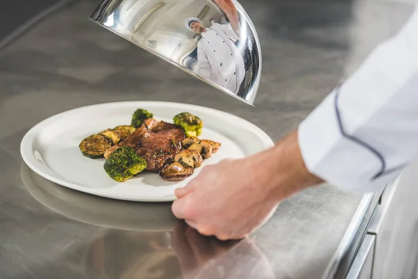 Image recadrée du chef tenant assiette avec repas et couvercle à la cuisine du restaurant — Photo de stock