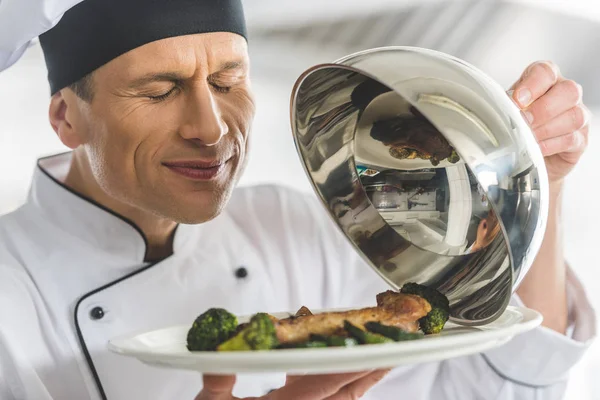 Chef bonito cheirando prato na cozinha do restaurante com olhos fechados — Fotografia de Stock