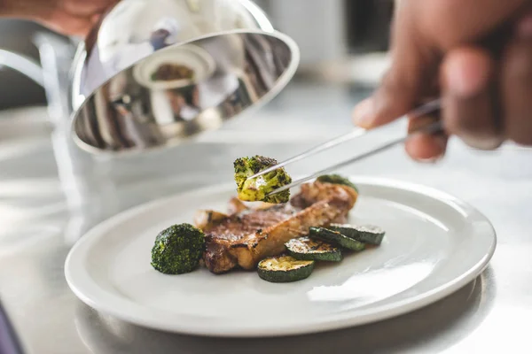 Image recadrée du chef afro-américain décoration assiette avec de la nourriture au restaurant cuisine — Photo de stock