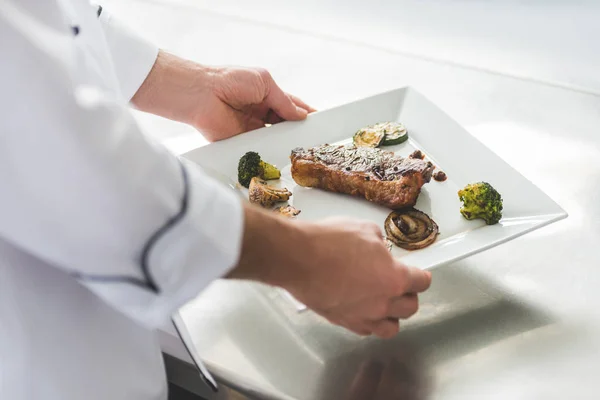 Imagen recortada del plato de la celebración del chef con filete cocido y verduras en la cocina del restaurante - foto de stock