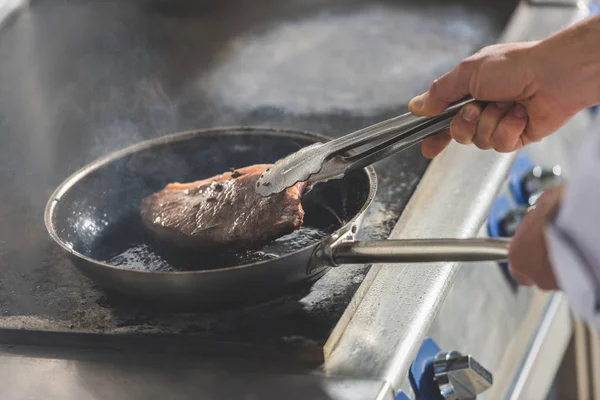 Обрезанный образ жарки стейка шеф-повара на кухне ресторана — стоковое фото