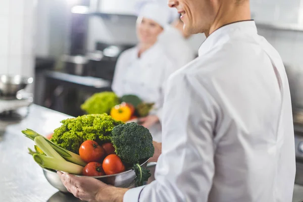 Abgeschnittenes Bild von Köchen, die Schüsseln mit Gemüse in der Restaurantküche halten — Stockfoto
