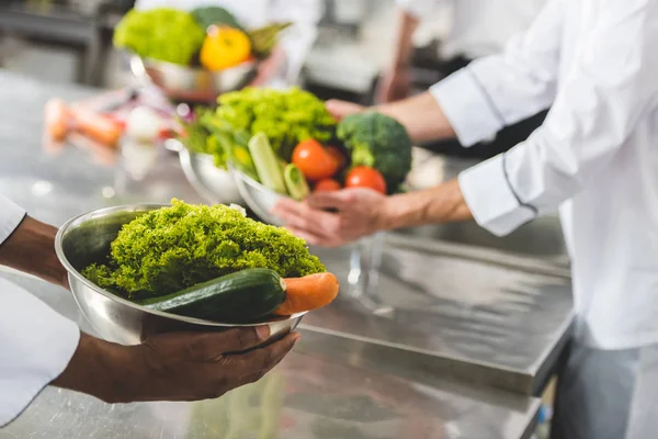 Immagine ritagliata di chef multiculturali che tengono ciotole con verdure in cucina ristorante — Foto stock