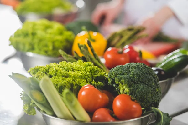 Обрезанный образ приготовления шеф-повара на кухне ресторана с спелыми овощами на переднем плане — стоковое фото