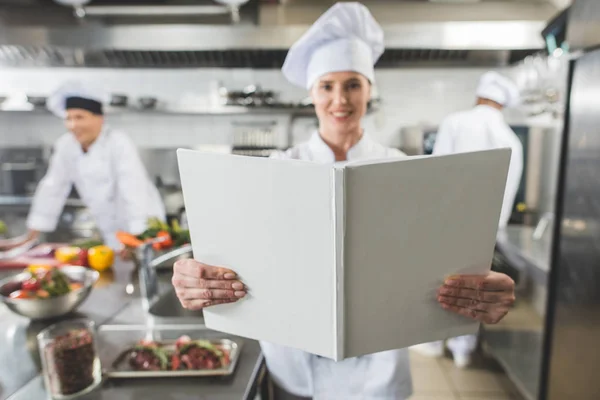 Smiling chef holding recipe book at restaurant kitchen — Stock Photo