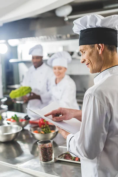 Chef apontando sobre livro de receitas na cozinha do restaurante — Fotografia de Stock